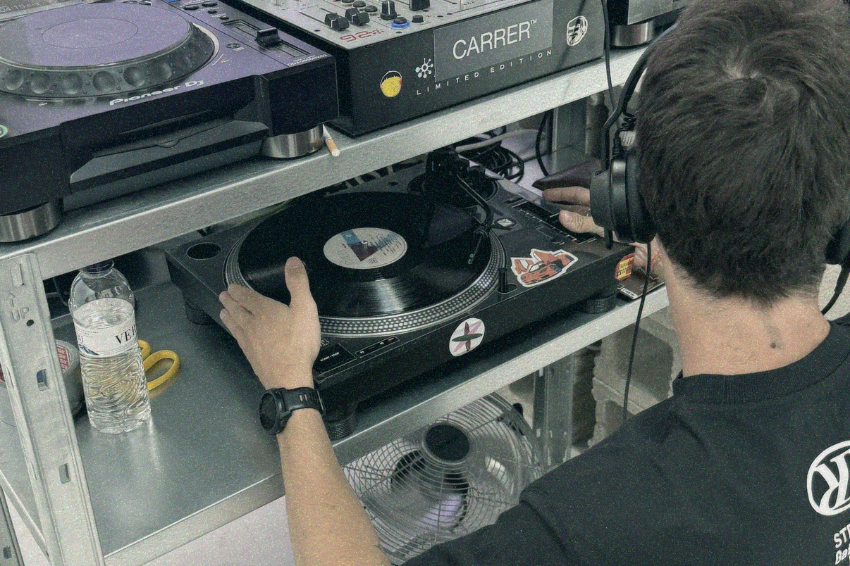 Mano sobre el vinilo en el Technics de la balda inferior; encima, un CDJ-2000NXS2 y la Xone:92 con el vinilo de CARRER